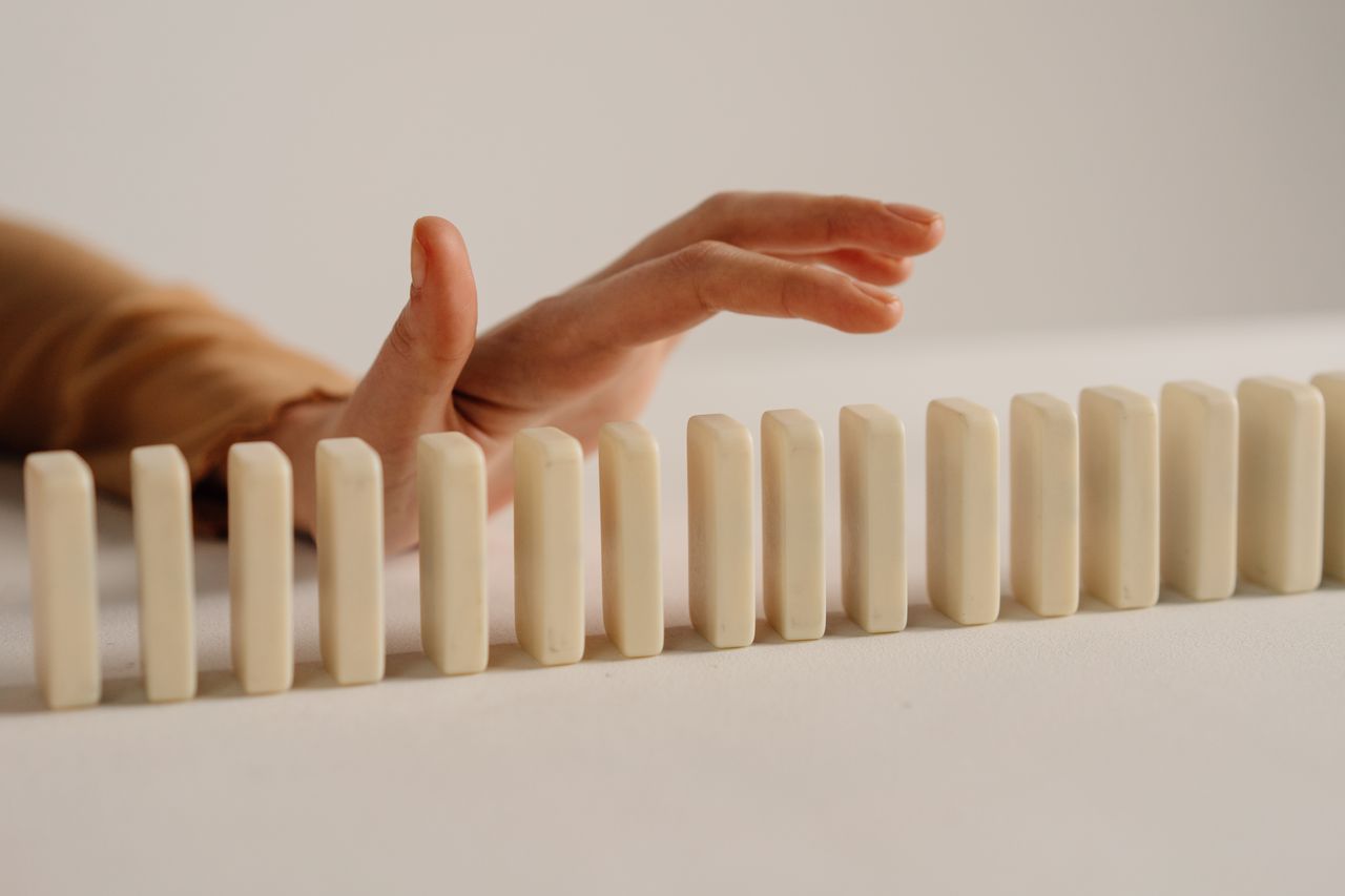 Home A hand poised to stop falling dominoes, depicting control and intervention.
