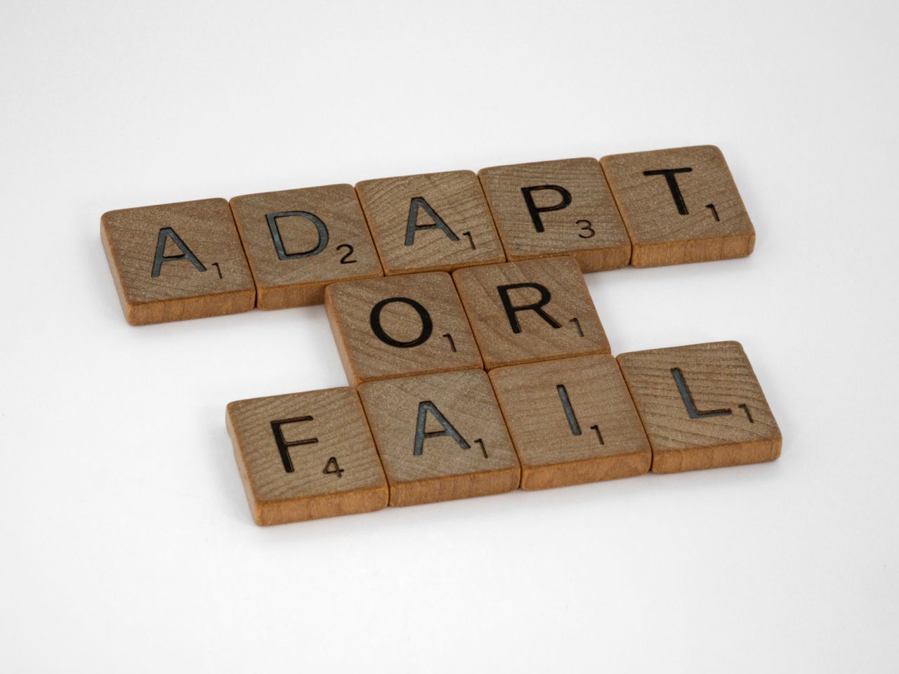 Scrabble tiles spell Adapt or Fail on a white background, conveying a motivational message.