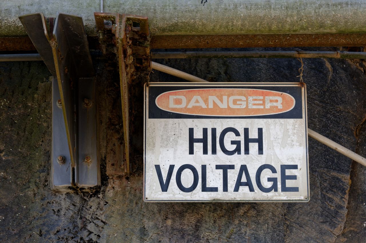 Home Rusty Danger High Voltage sign on an outdoor wall, indicating electrical hazard.